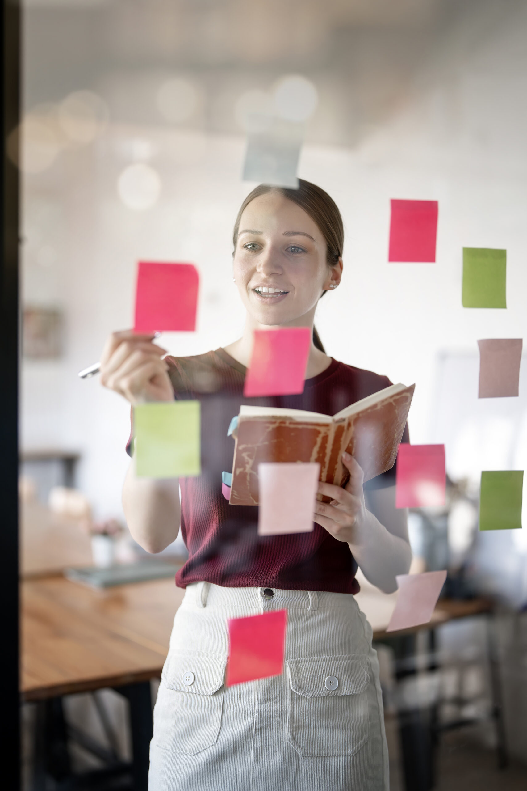 Young smiley attractive businesswoman using sticky notes in glas